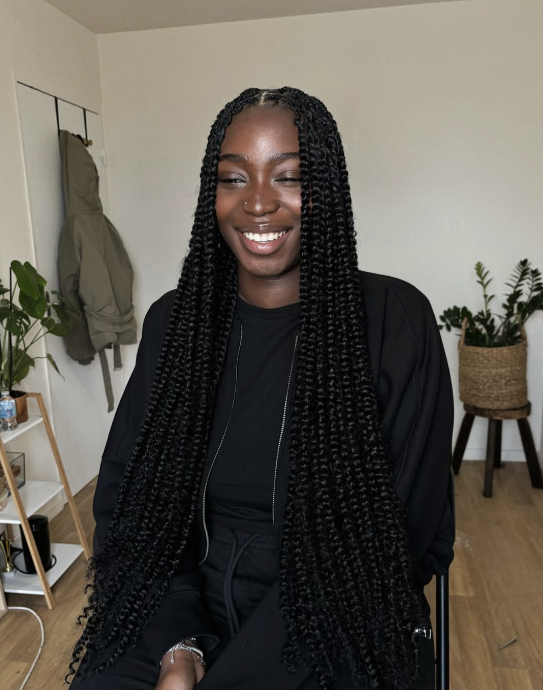 A woman smiling while wearing long, curly-textured passion twists with a middle part, styled with a black zip-up hoodie.