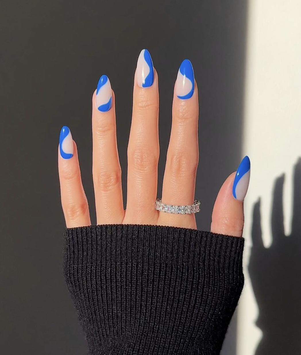 Long, oval-shaped nails featuring a translucent, bare base accented by fluid, abstract waves of vibrant cobalt blue and crisp white polish.