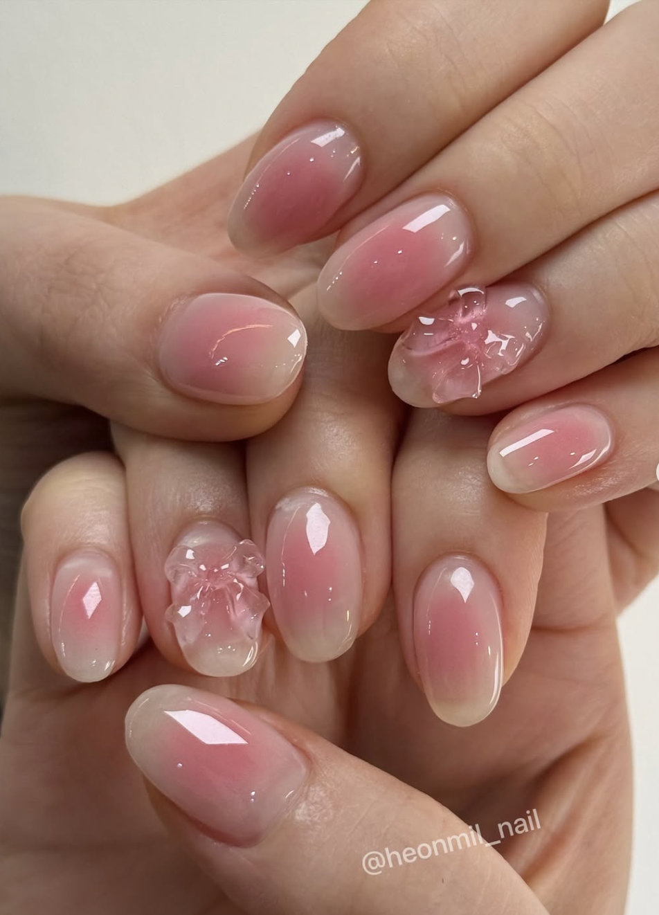 Long almond-shaped nails with a translucent "jelly" pink gel finish, featuring a high-shine glassy top coat and delicate 3D floral accents on the ring finger.