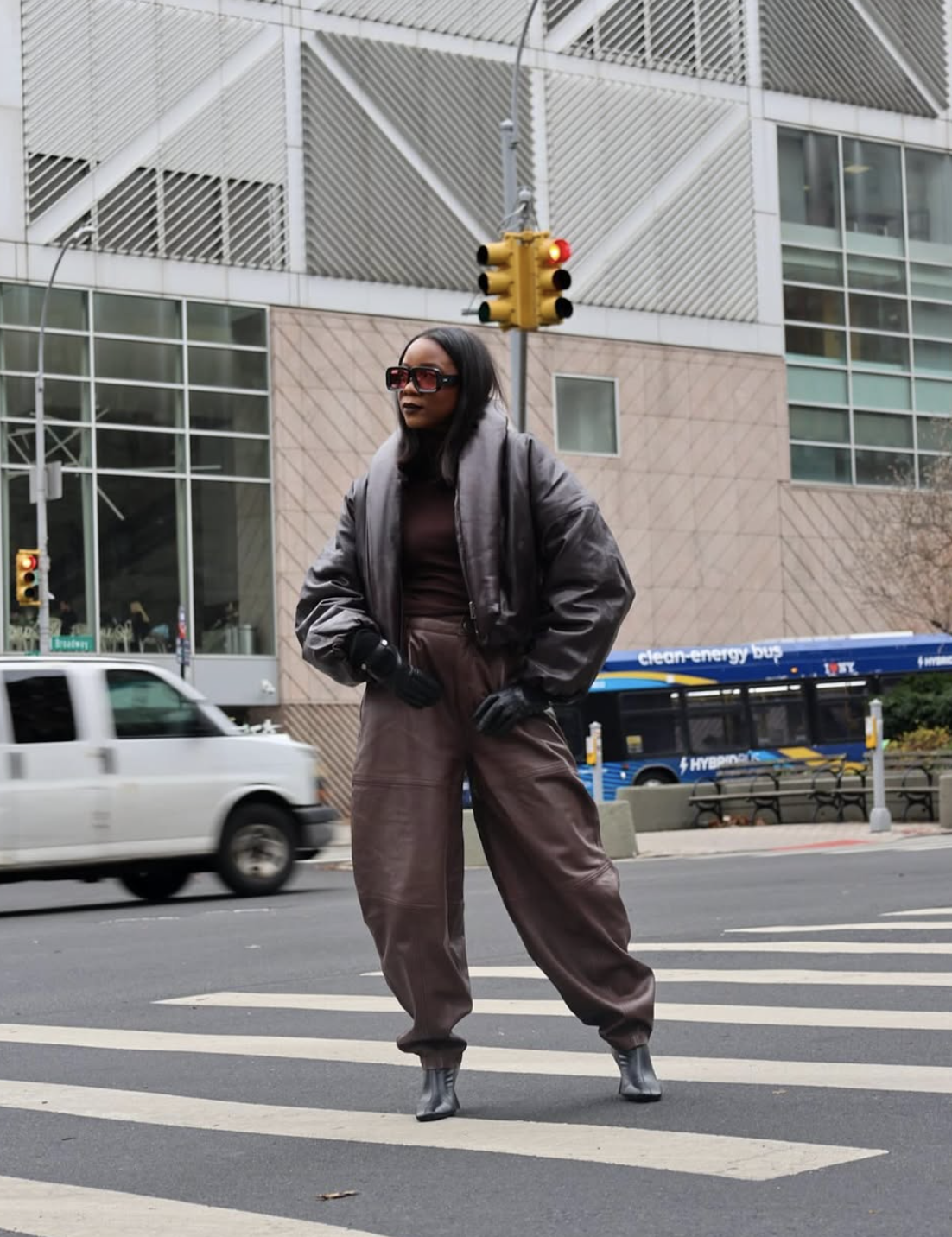Woman wearing brown leather jogger pants, a burgundy top and a black leather puffer jacket on a city street