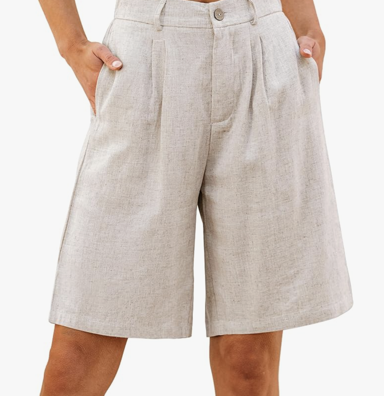 A close-up of a woman's hand in the pocket of tan high-waisted linen Bermuda shorts featuring vertical pleats and a structured waistband.