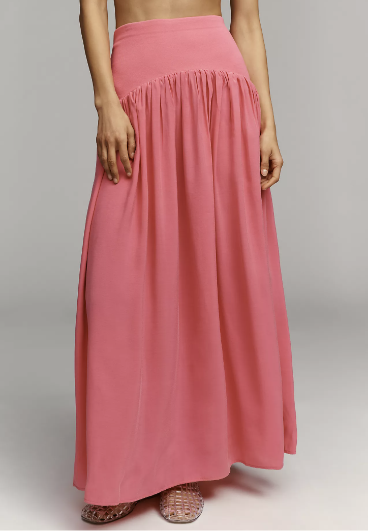 Close-up of a vibrant pink maxi skirt with a gathered waistband, paired with silver metallic woven flat sandals.