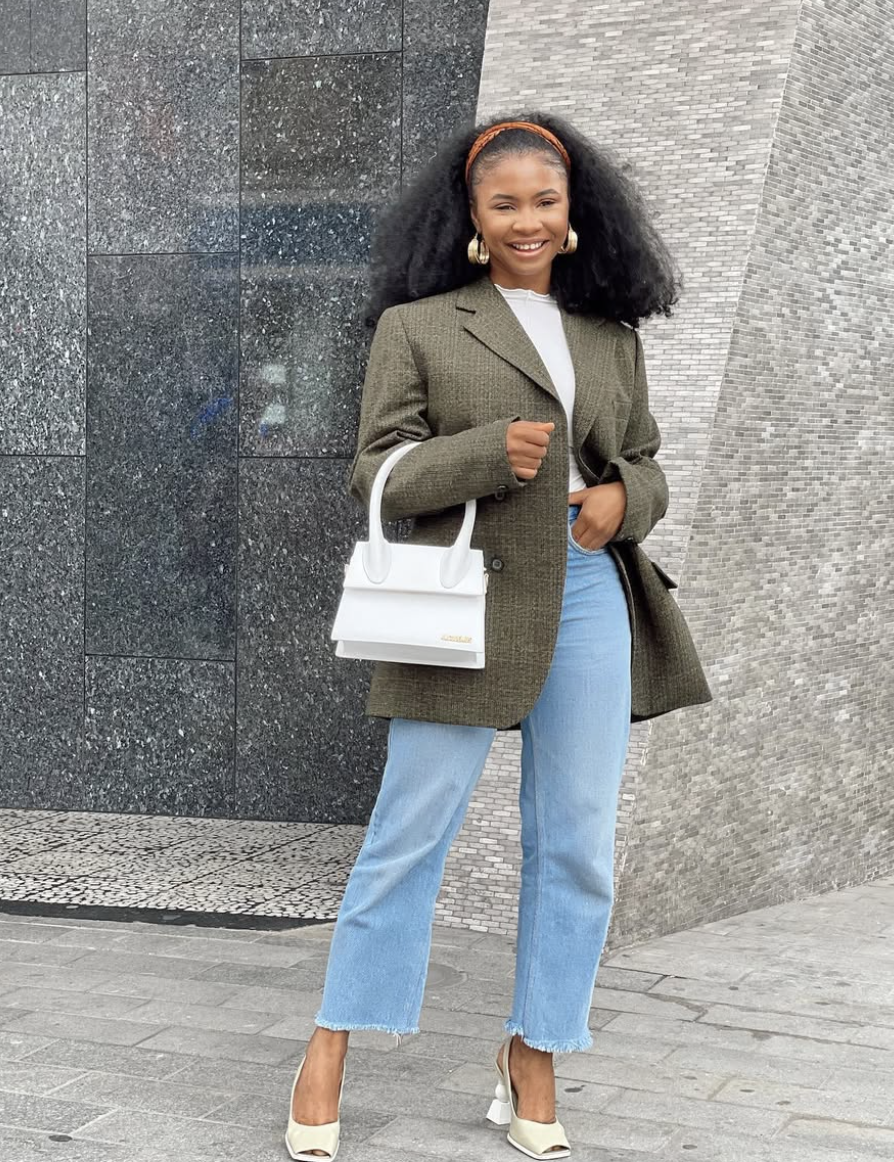 A woman wearing a grey textured wool blazer over a white top and light wash jeans, holding a white structured handbag for a chic street-style look.