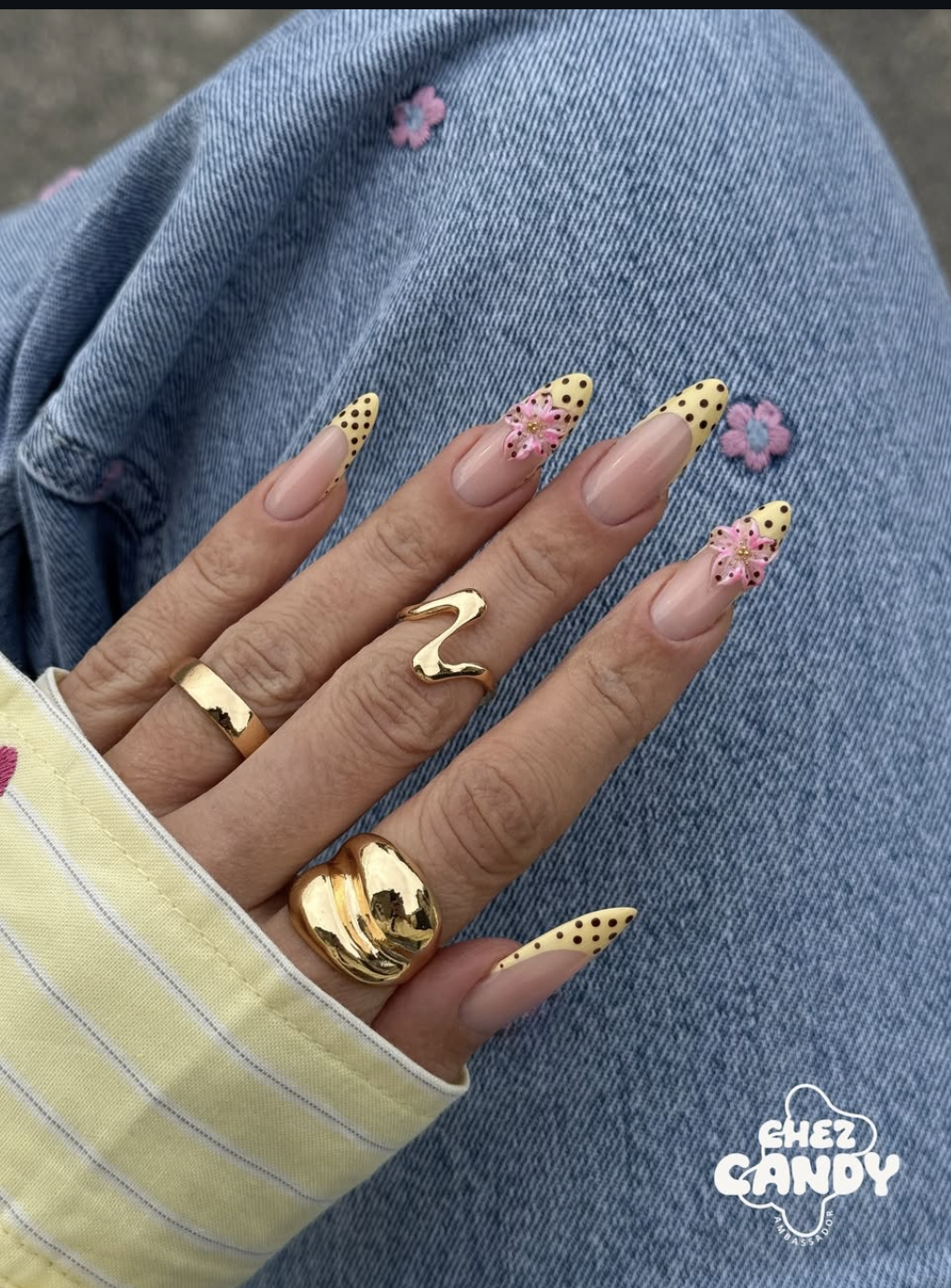 Long almond nails with polka dot French tips and a 3D pink flower accent.