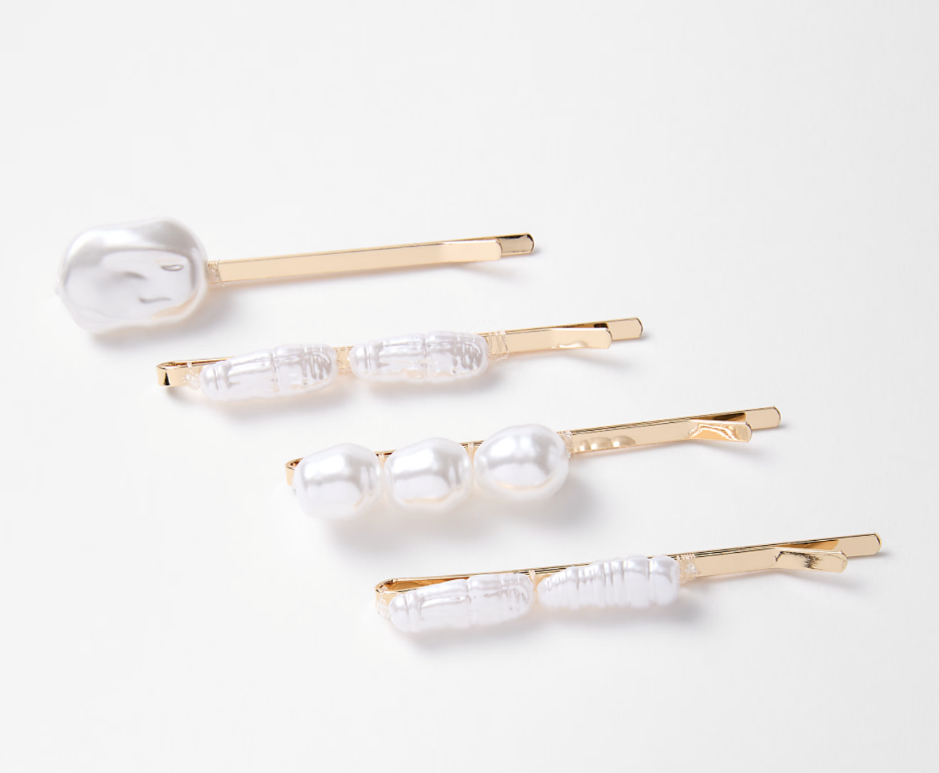 Four gold bobby pins decorated with pearl beads on a white background