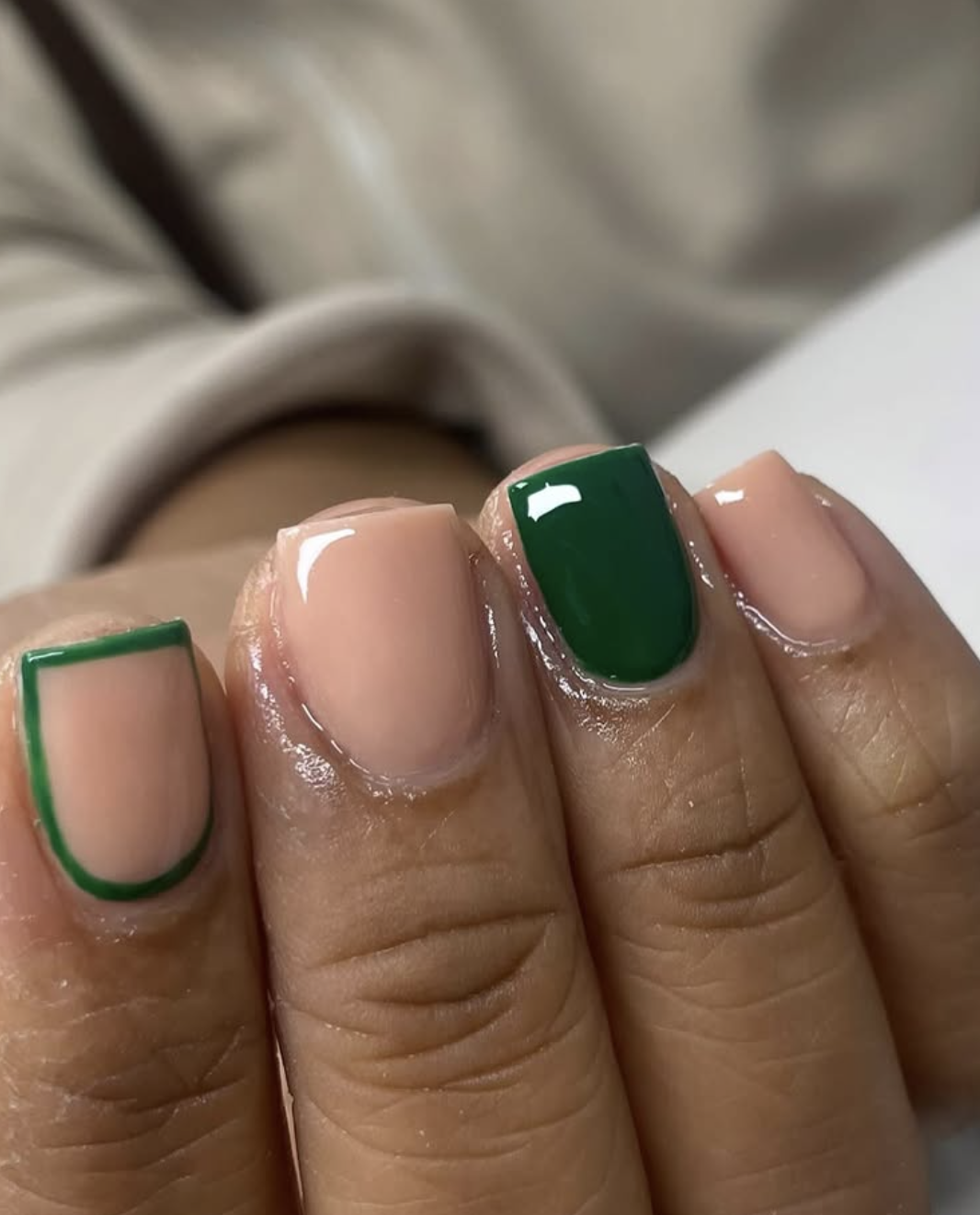 Short square nails with a glossy nude base featuring a forest green solid accent nail and a matching green minimalist French outline design.
