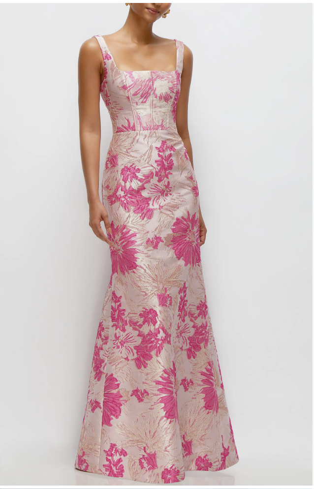 A woman wearing a structured, floor-length column gown in a vibrant pink and metallic gold floral jacquard fabric, featuring a square neckline and wide shoulder straps.