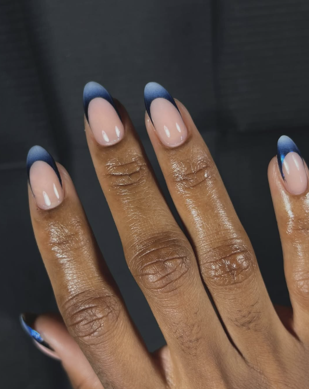 Long almond shaped nails with a nude base and deep midnight blue French tips.