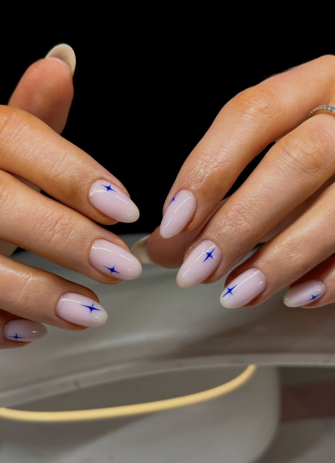 Long, almond-shaped nails featuring a crisp white French manicure base upgraded with delicate hand-painted gold starbursts and tiny metallic dots