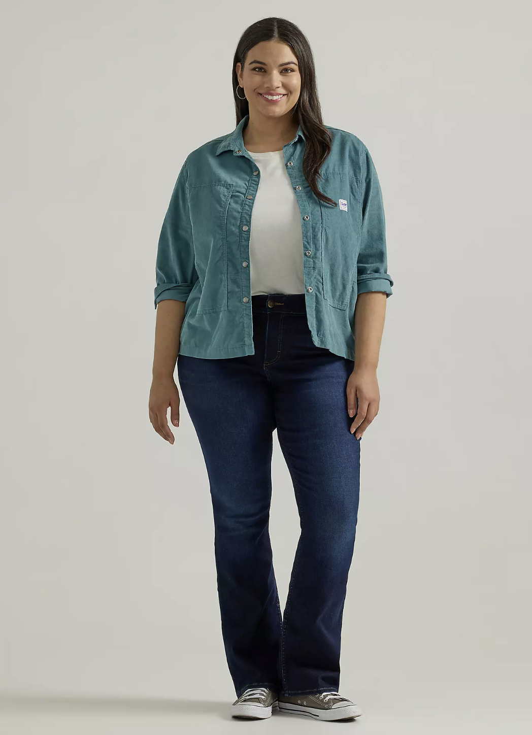 A person smiling and wearing dark wash Lee Ultra Lux Comfort Bootcut jeans, styled with a white t-shirt and an open teal button-down shirt.