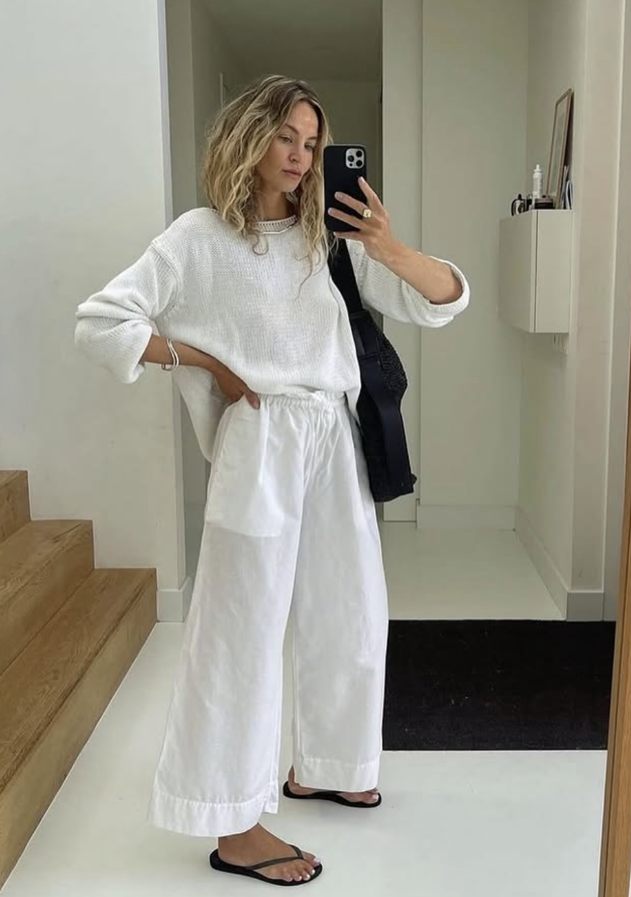 A person wearing a white wide-leg linen matching set with flat black leather flip flops.