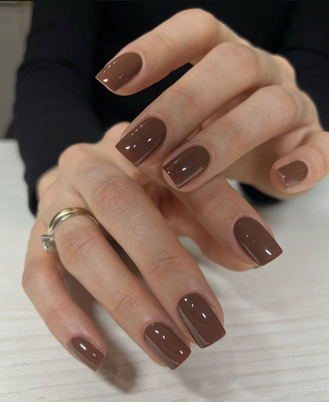 A deep chocolate brown Italian manicure on short natural nails, painted with a narrow unpainted gap along each sidewall to elongate the nail.