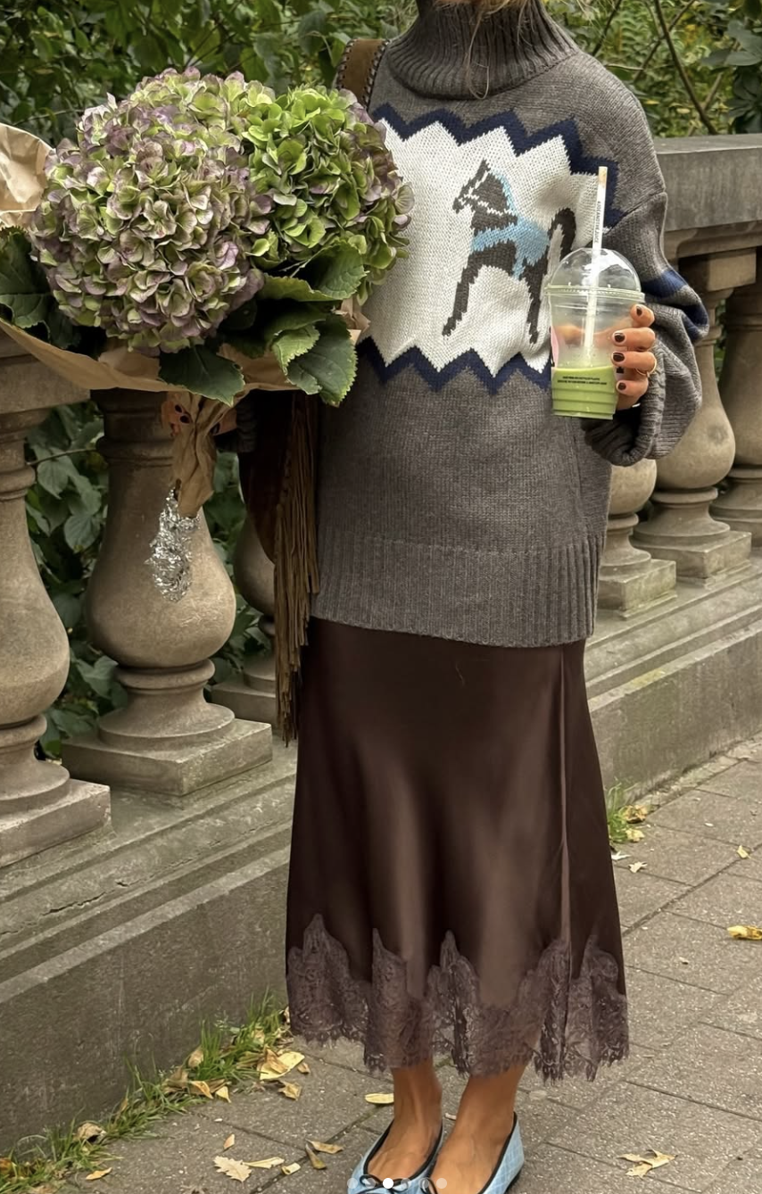 A pro stylist-inspired layering look featuring a chunky grey crewneck sweater layered over a brown satin slip dress with lace trim.
