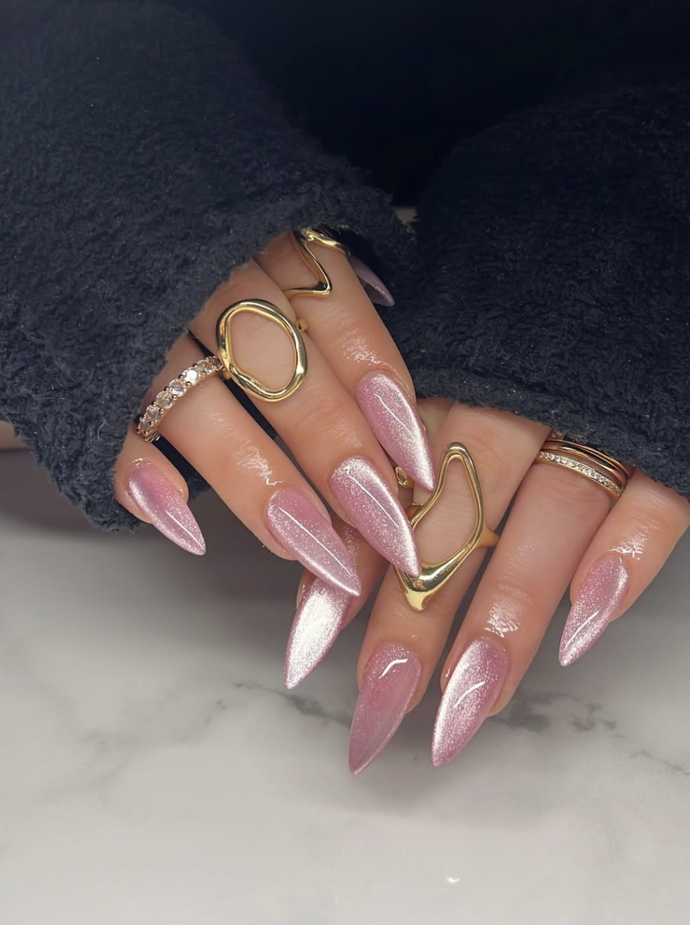 A close-up of natural-shaped nails with a soft rose pink chrome finish and a pearlescent, shimmering reflection.