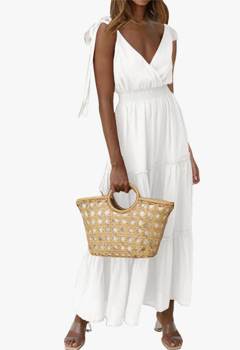 A woman wearing a white cross-neck sleeveless tiered midi dress, styled with a woven straw tote bag for a summer outfit idea.