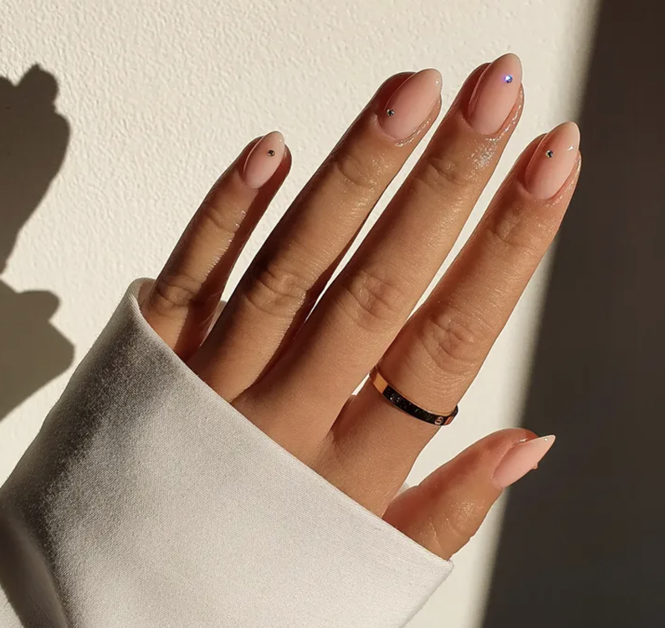 Medium almond-shaped nails with a glossy nude base coat featuring a single tiny black rhinestone accent centered near the cuticle of each nail.