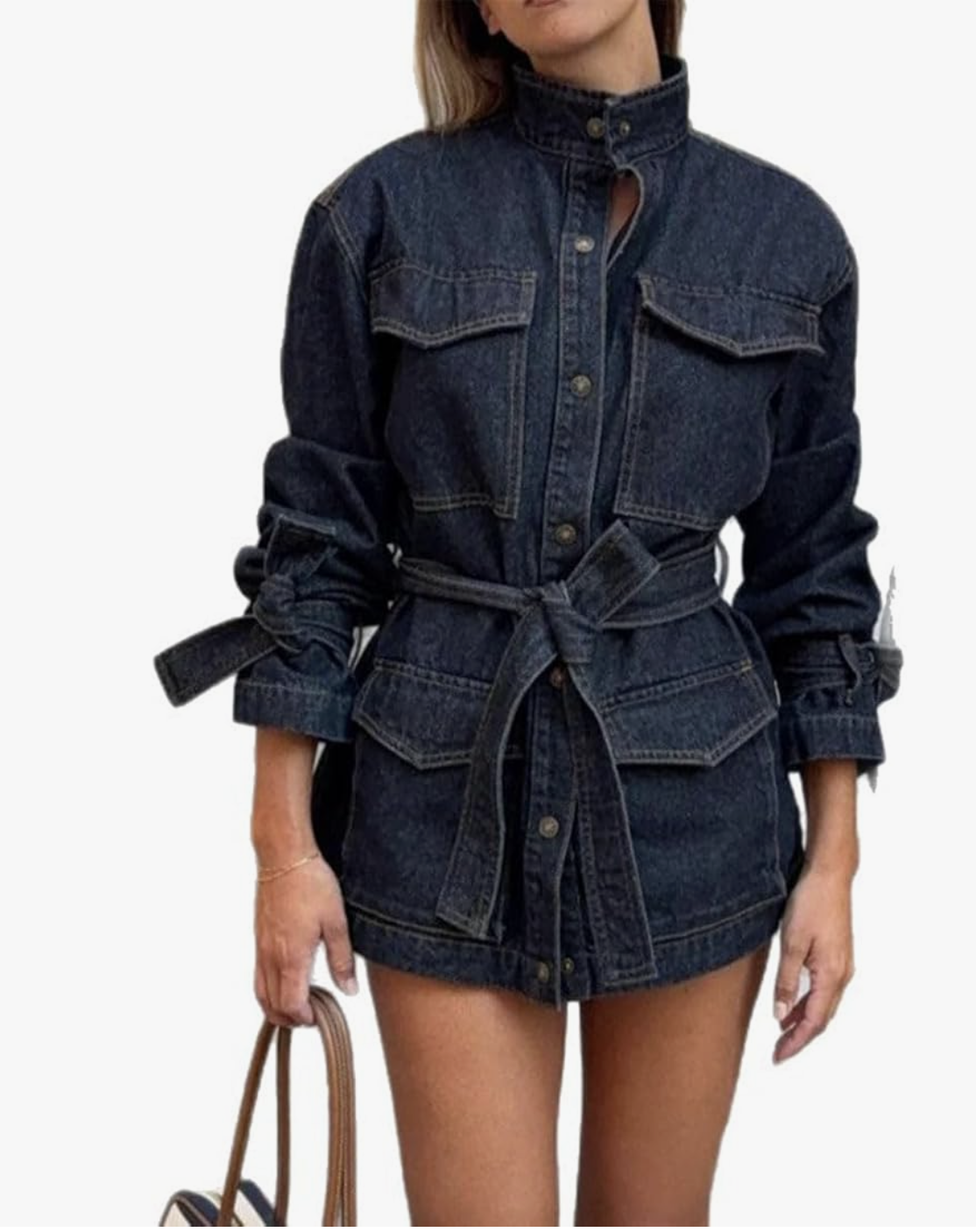 A woman wearing a dark-wash belted denim utility jacket with a high collar and oversized pockets, styled as a polished layering piece for a spring capsule wardrobe.