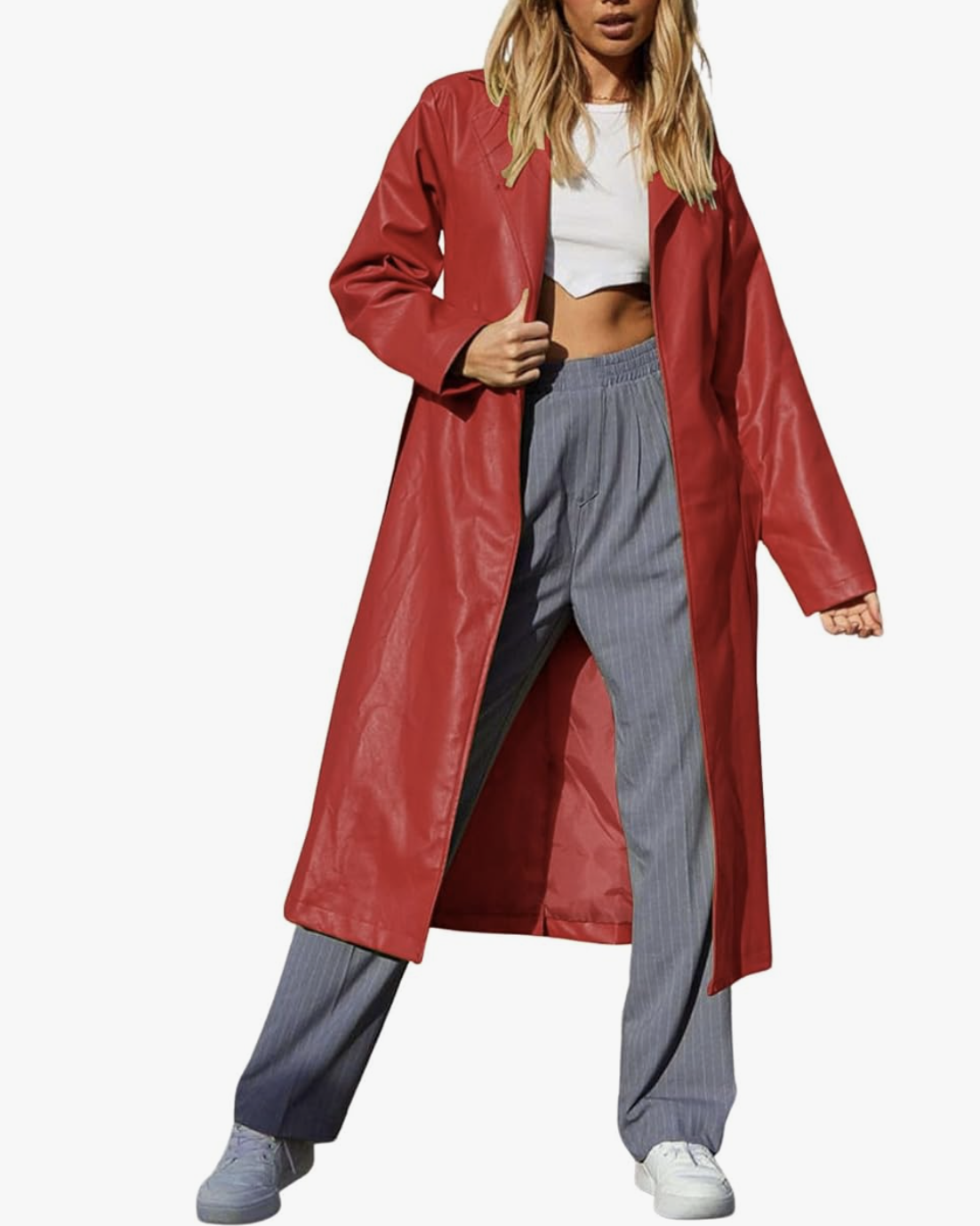 A vibrant red faux leather long trench coat with a structured collar and belted waist, styled over grey pinstripe trousers and a white crop top for a modern spring outfit.
