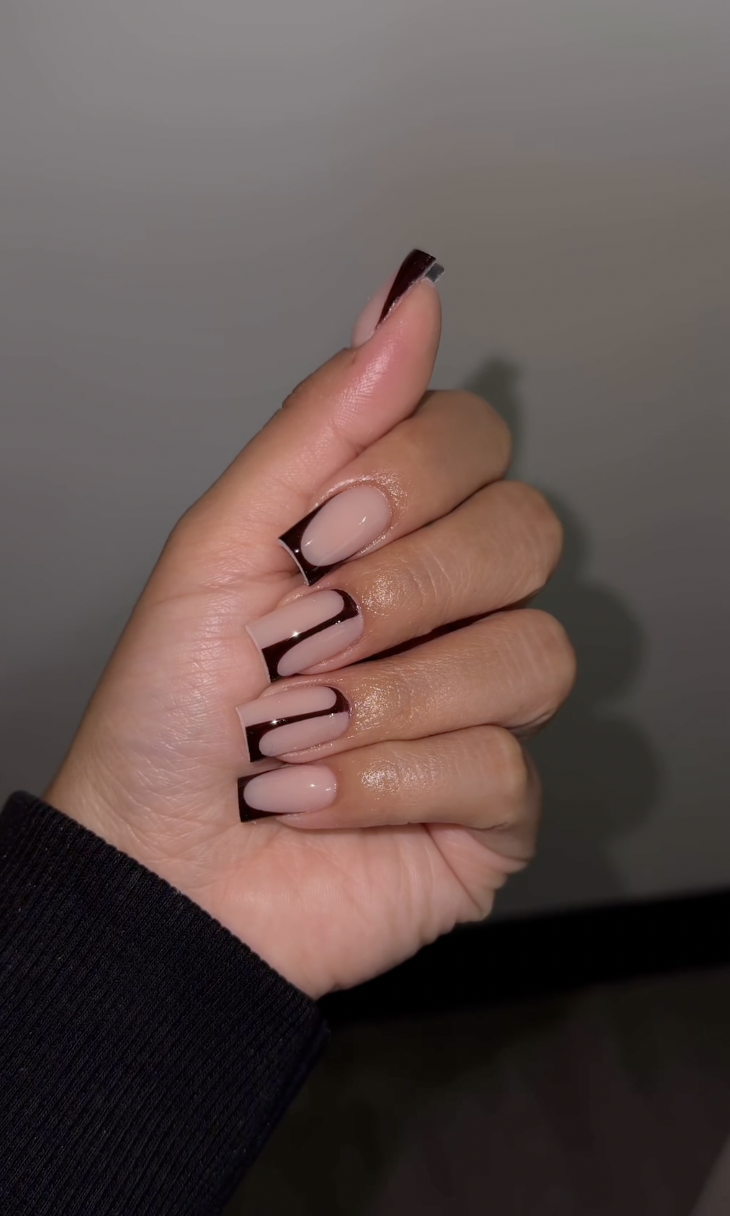 Close-up of a hand featuring an espresso dark brown micro French manicure with thin tips and a swirl accent nail over a sheer nude base.