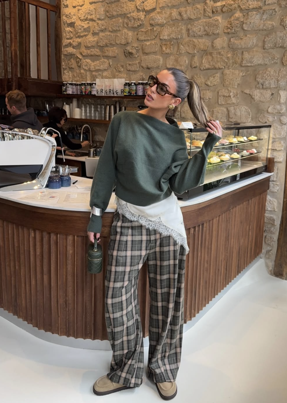 A woman wearing a monochromatic forest green outfit featuring a textured knit sweater layered over a lace-trim top and plaid wide-leg trousers.