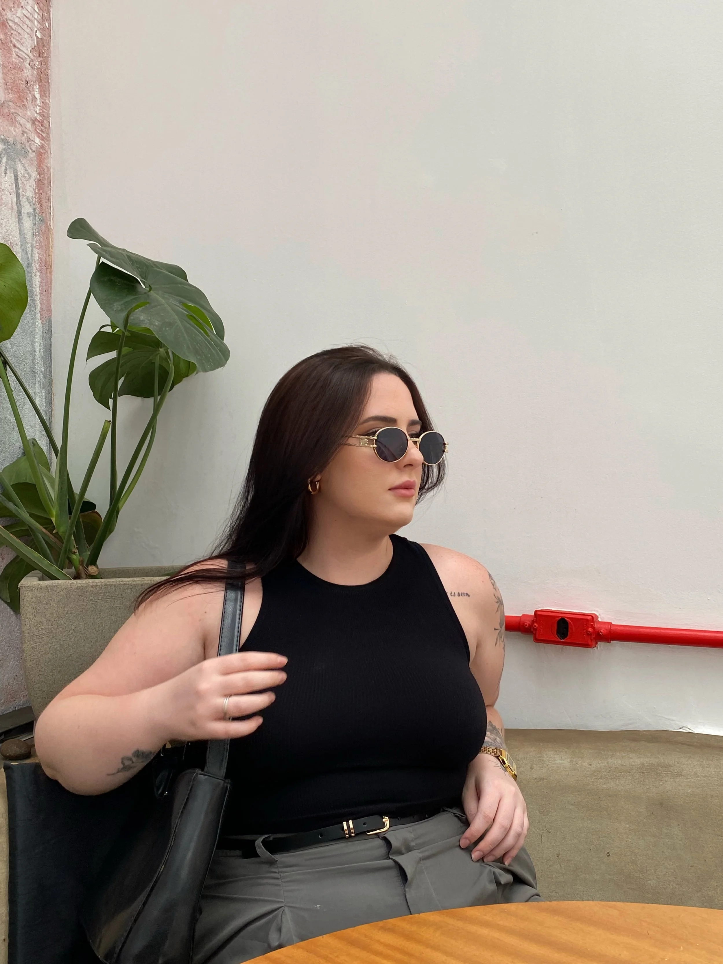 A woman with long dark hair and sunglasses wearing a black high-neck tank top and grey trousers, styled as a designer-inspired minimalist spring outfit from Amazon.