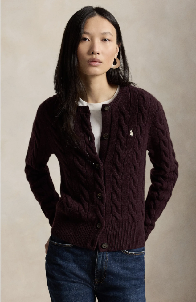 Model wearing a plum purple cable-knit button-up cardigan paired with dark-wash jeans on a white background.