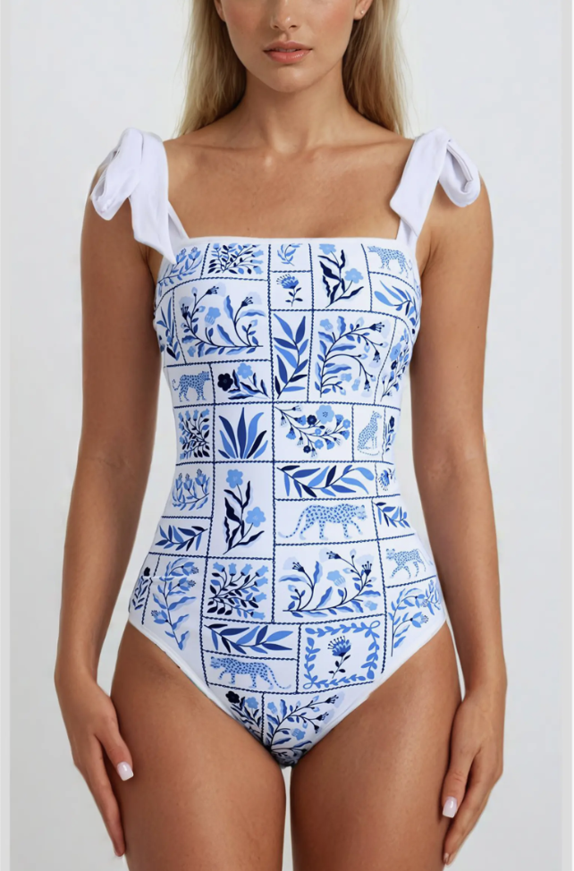 A close-up of a women's square-neck swimsuit in a blue and white tile print with shoulder tie details, styled for a vacation wardrobe.
