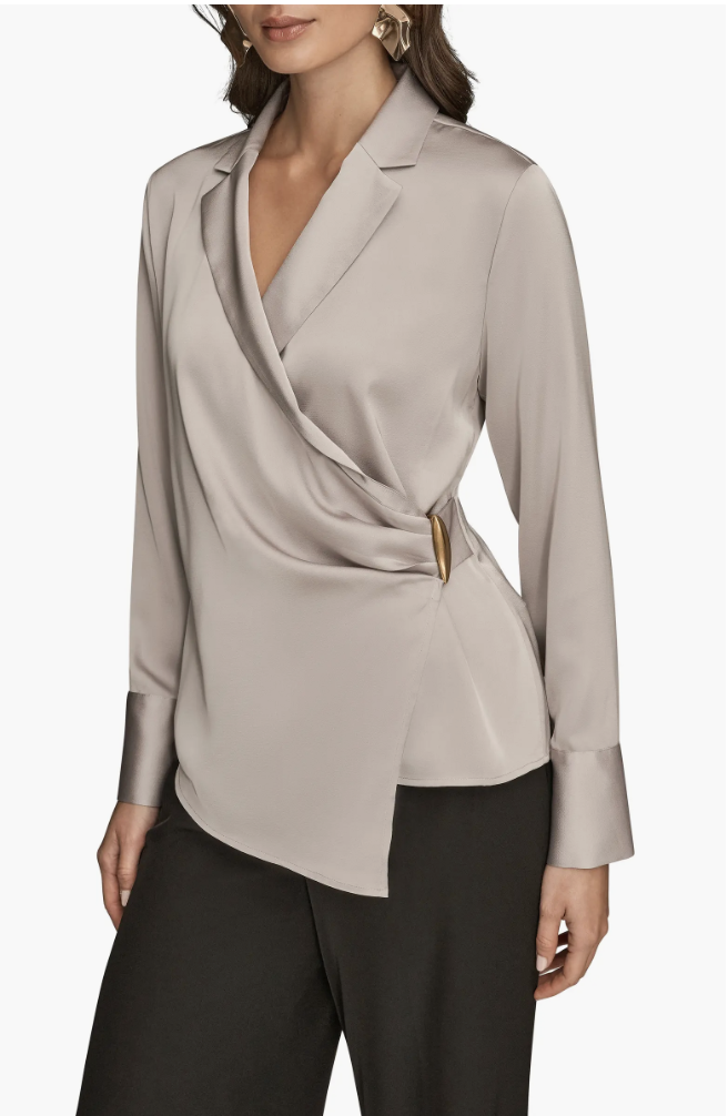 A woman wearing a Donna Karan New York grey silk top with a pleated wrap-front design and a gold circular buckle detail, paired with black trousers for a professional office capsule wardrobe.