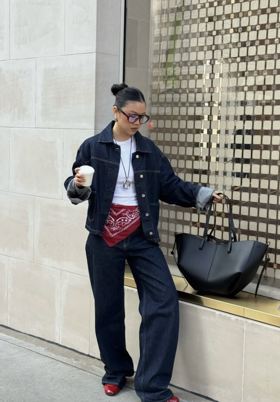 An oversized double denim outfit consisting of a denim jacket and wide-leg puddle jeans, accented with a red printed bandana used as a scarf belt and matching red ballet flats.
