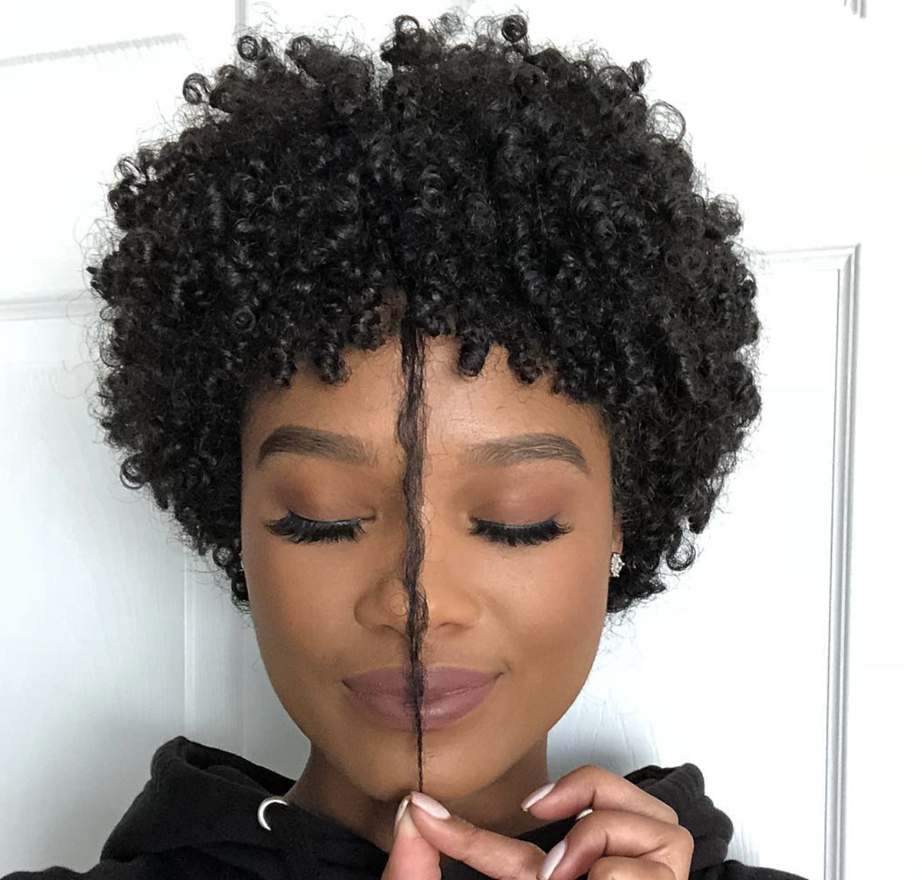 Lyssa Marie with a short, rounded natural curly haircut and a single curl falling forward, highlighting a diamond face shape and sharp bone structure.