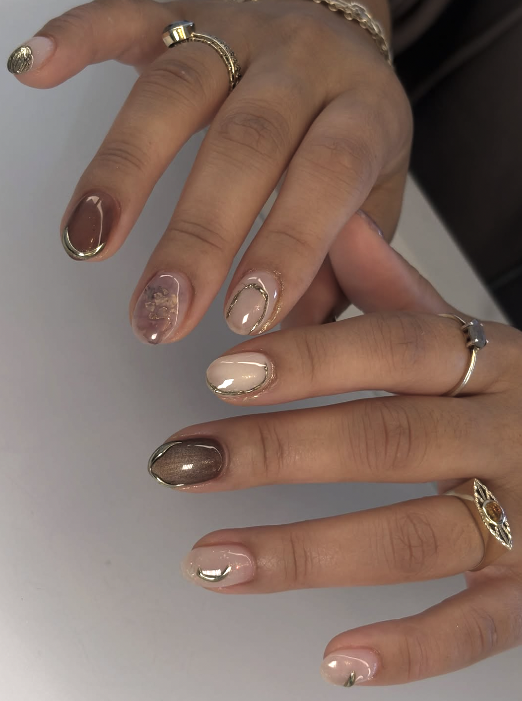 Close-up of a hand with short, rounded nails featuring a mix of neutral brown, beige, and gold metallic accents