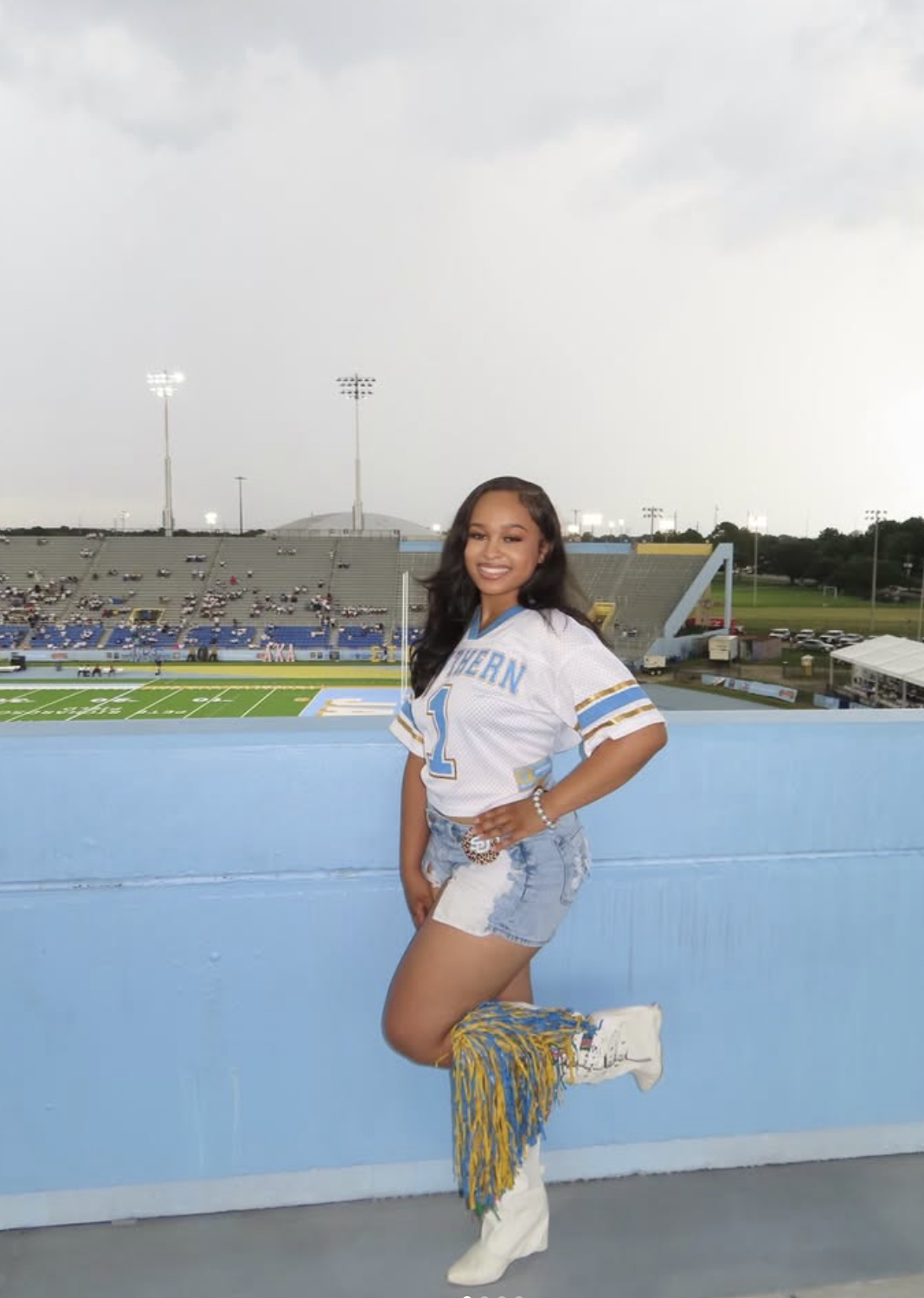 Woman at a college football game wearing a cropped blue-and-white jersey, denim shorts and white cowboy boots.