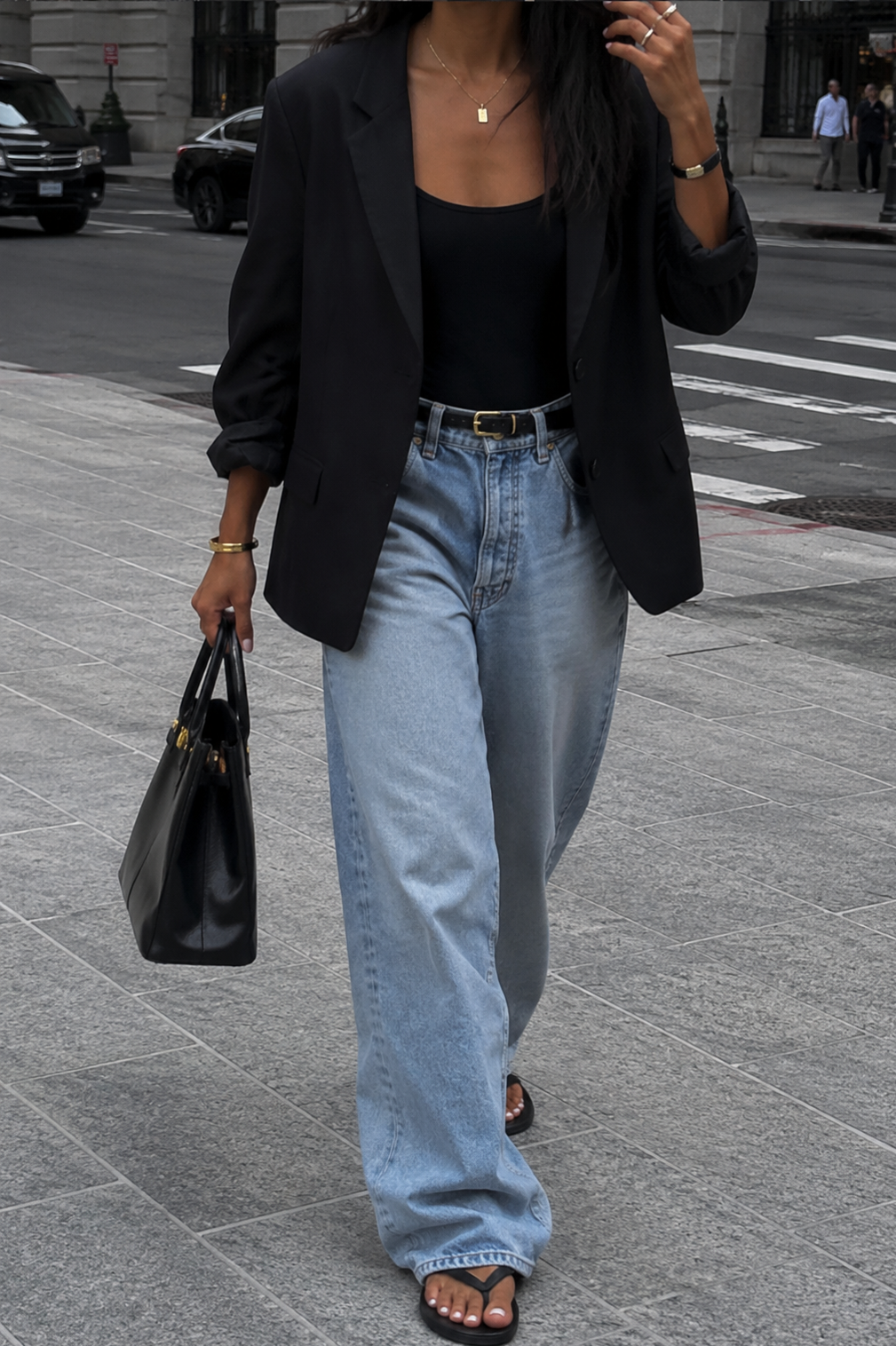 A person wearing straight-leg light-wash denim and black supportive sandals walking on a sunlit city sidewalk.