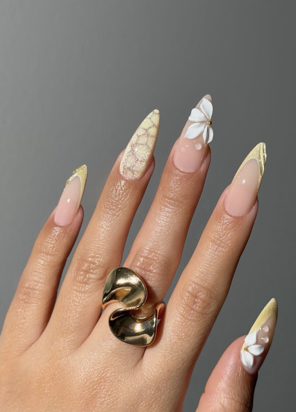 A luxurious high-feminine spring manicure by @klawsbysonia featuring buttery yellow nails, a large 3D white sculptural flower with a gold center, and intricate gold foil textured accents.