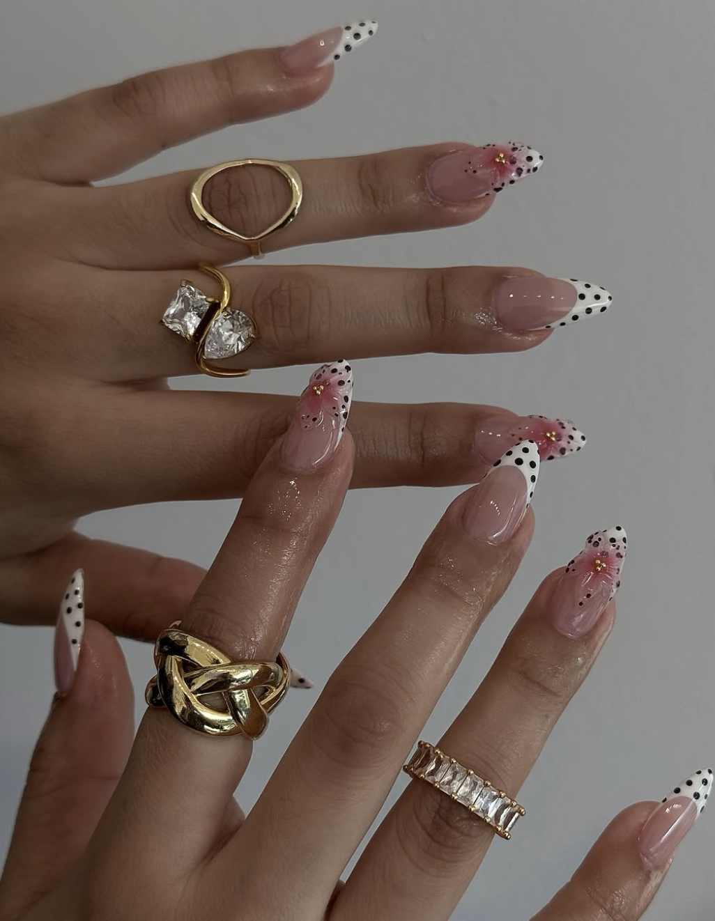 Long almond nails with white French tips, gold foil accents, butterfly wing nail art, and a 3D pink flower.