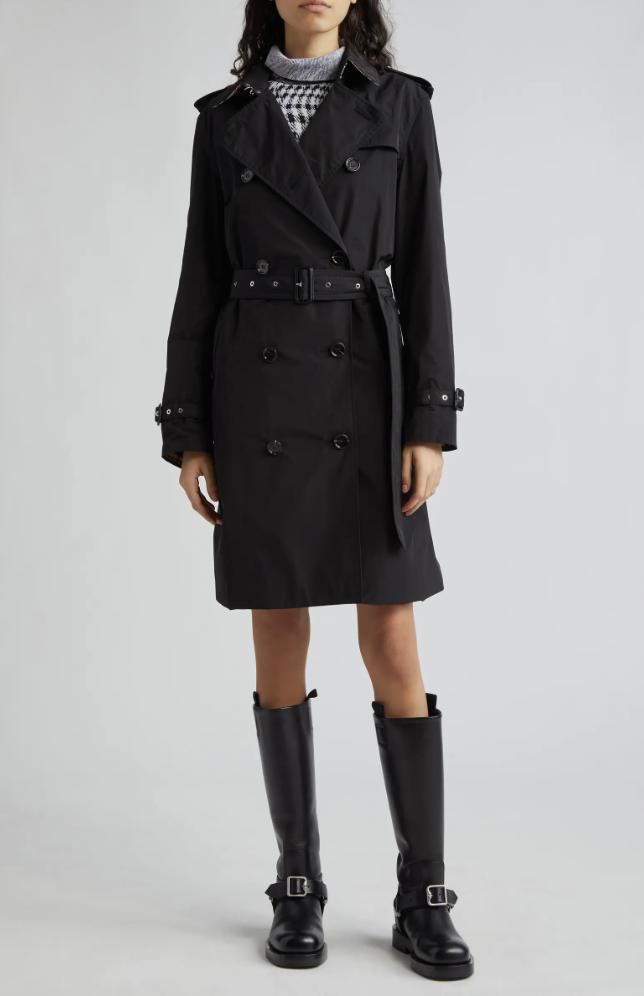 The Burberry Kensington Heritage trench coat in black, featuring a double-breasted front and belted waist, styled with chunky black leather moto boots for an edgy luxury look