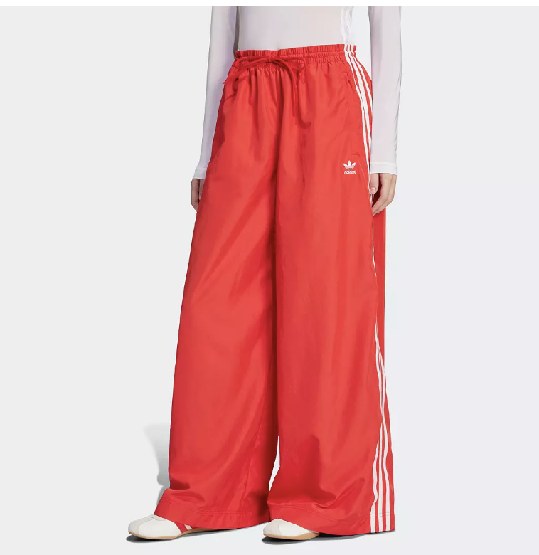A front-facing view of the red Adidas Originals Adilenium track pants featuring an ultra-wide-leg silhouette, white side stripes, and a drawstring waist for a high-fashion Sportif Luxe look.