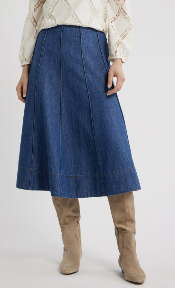 A woman wearing a dark wash denim midi skirt with an A-line silhouette paired with light beige suede knee-high boots.