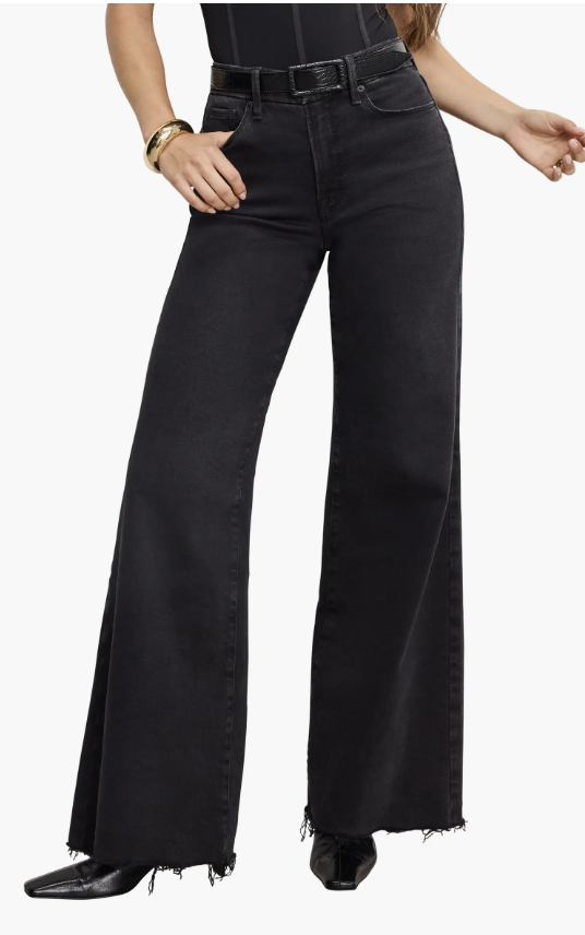 A person wearing black Good American Good Waist Palazzo jeans with a raw hem and a dramatic wide-leg flare, demonstrating a gap-proof fit on an hourglass figure