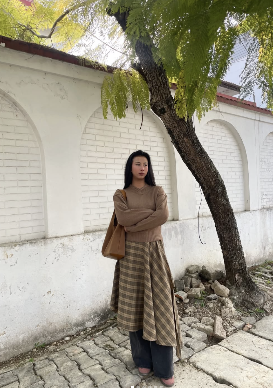 A pro stylist-inspired outfit featuring a tan plaid dress layered over dark wide-leg trousers and a brown sweater.