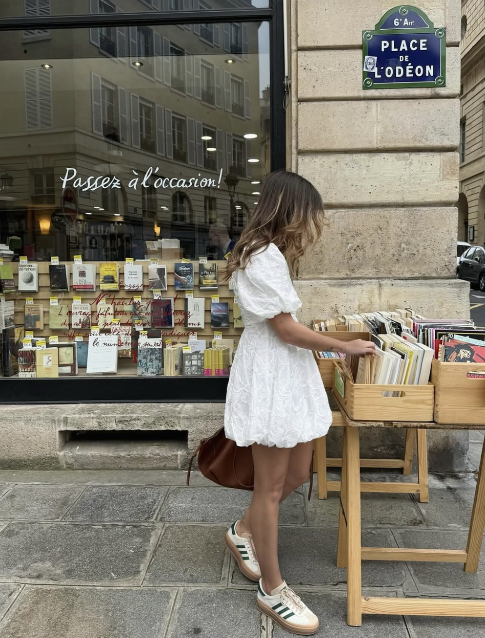 A person wearing a dark babydoll dress paired with brown leather loafers and cream-colored ankle socks, sitting on a wooden bench.