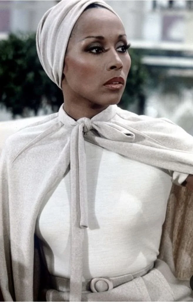 Classic style icon Diahann Carroll wearing a structured white high-neck blouse and matching headwrap, illustrating timeless elegance and polished monochromatic fashion."