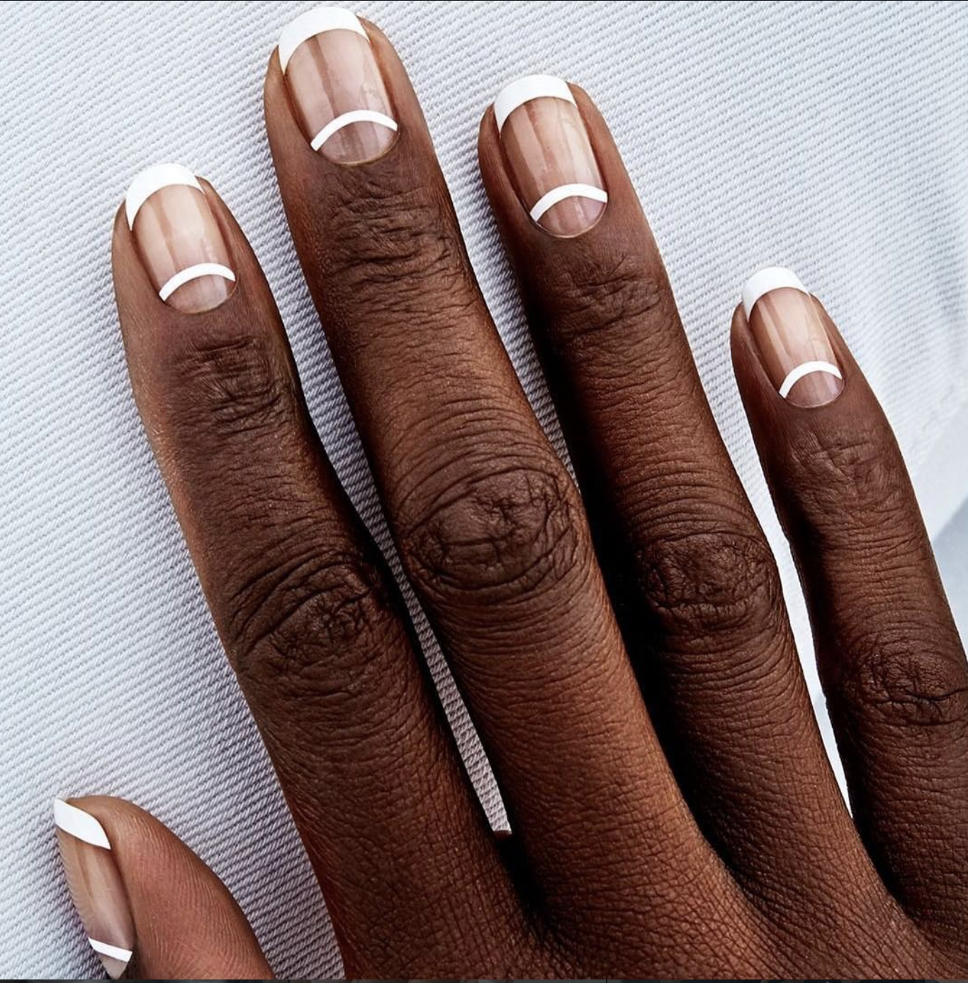 Short burgundy nails with clean negative-space half moons at the cuticles.