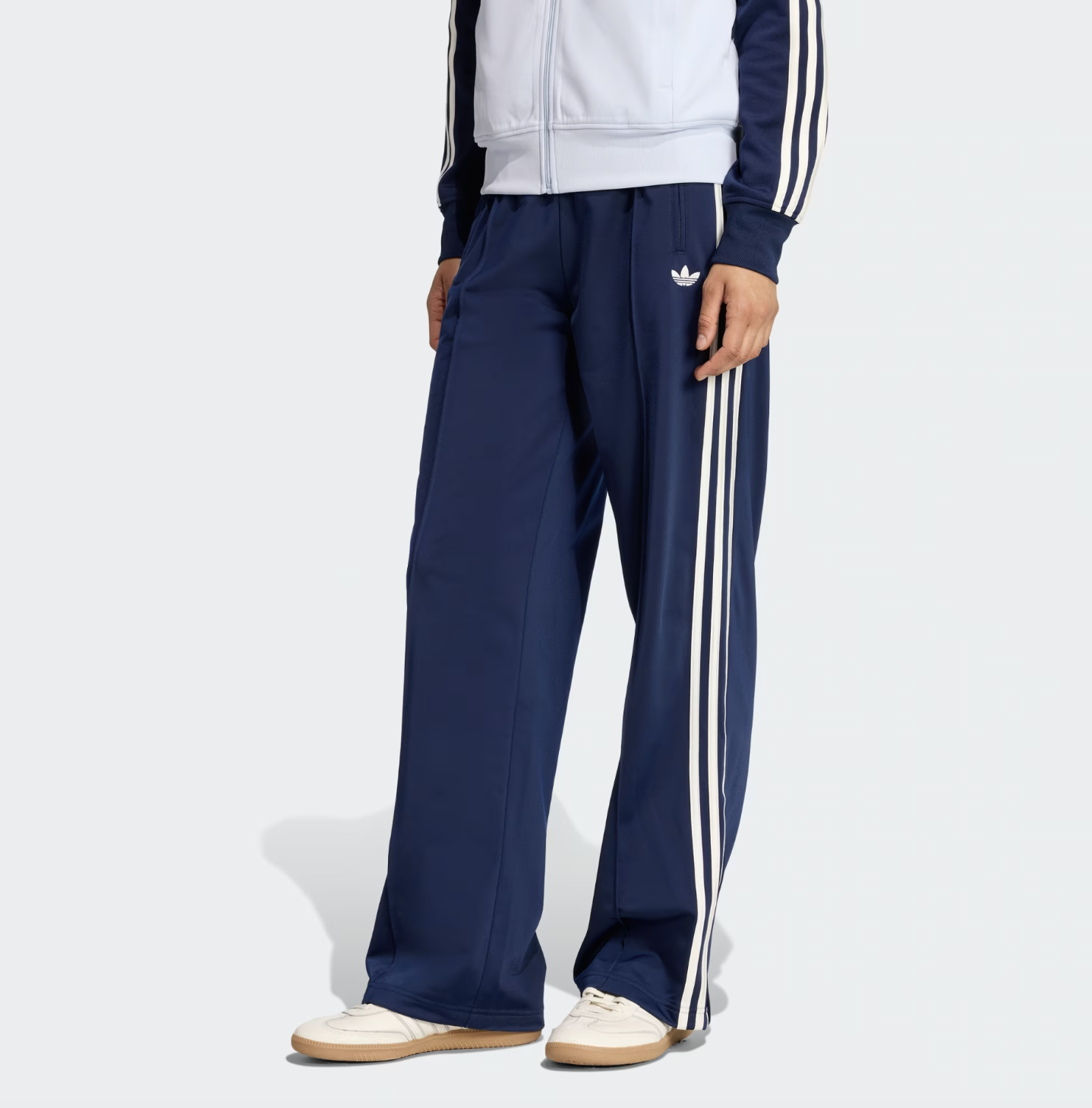 A pair of navy blue Adidas FB Loose Track Pants featuring the iconic white triple stripe and Trefoil logo, demonstrating a wide-leg sporty silhouette for a luxury streetwear look.