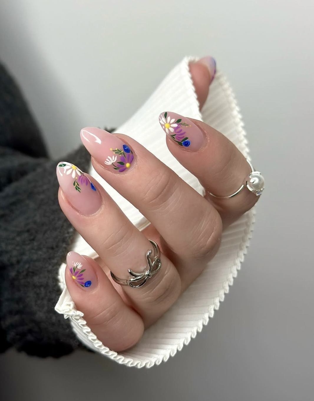 Long almond-shaped nude nails featuring detailed, colorful hand-painted wildflowers in shades of blue, purple, and yellow.