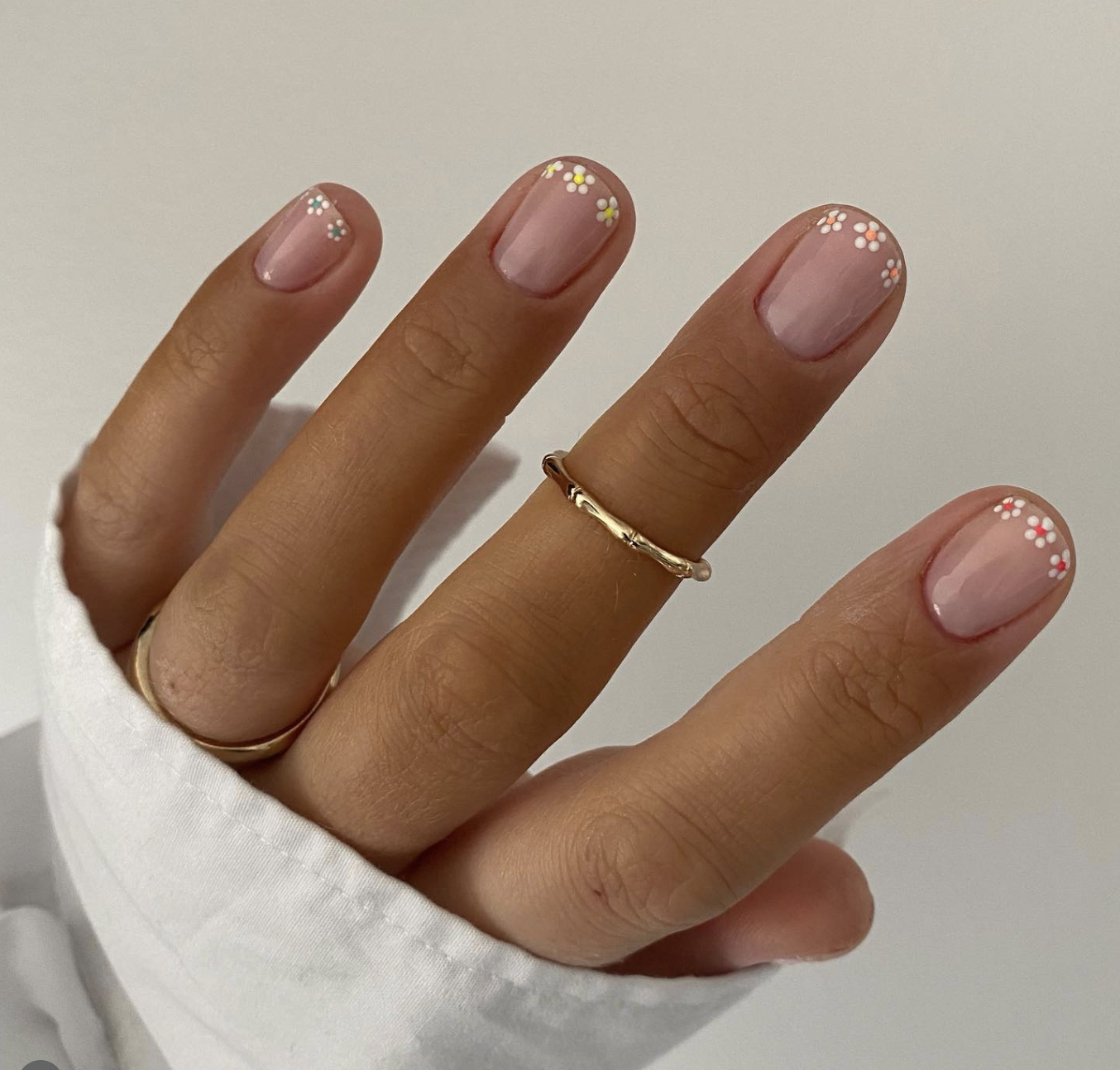 Short squoval nails with a glossy pale pink base coat featuring minimalist white and yellow daisy accent flower designs at the cuticles and tips.