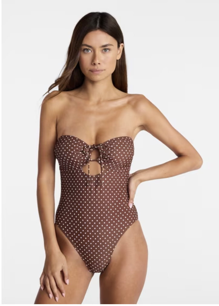 A close-up view of a woman wearing a high-cut chic brown one-piece swimsuit with a classic white polka dot pattern.