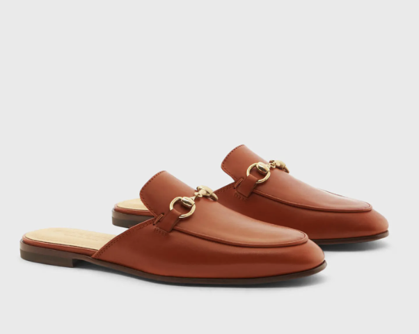 Cognac brown leather backless bit loafers with a gold buckle hardware detail on a white background.