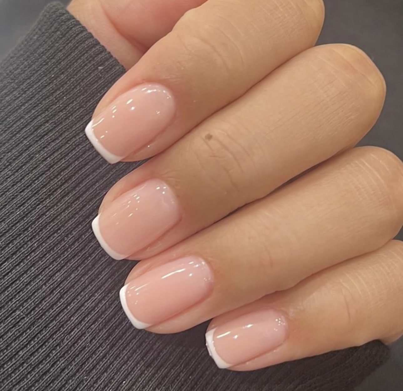 Hand wearing Modelones extra-short squoval French tip press-on nails with a sheer pink base and white tips.