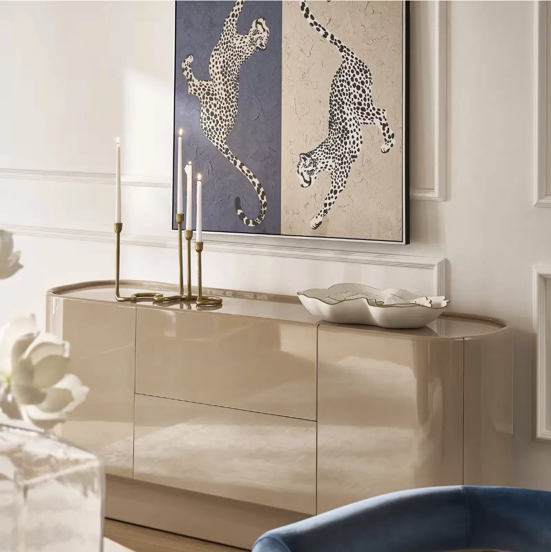A large cheetah print canvas wall art framed above a light wood console table styled with tall gold taper candlesticks and decorative white bowls.